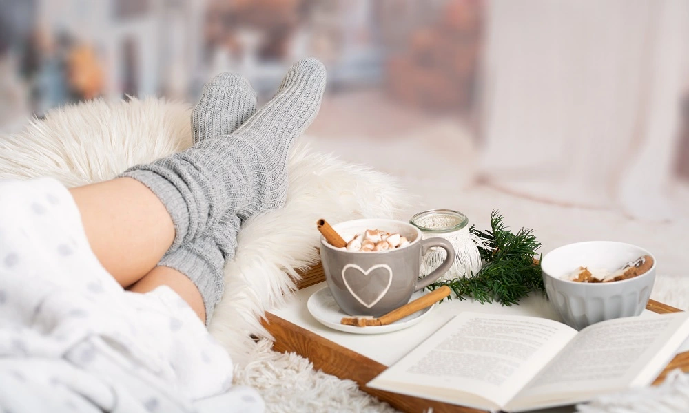 Frauenfüsse mit dicken Socken und einer heissen Schokolade in gemütlicher Atmosphäre